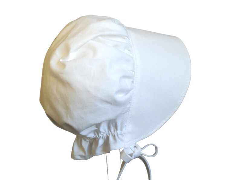 White prairie bonnet with wide brim facing right. Some of the bonnet back is showing. The side-back is puffy and gathered onto the brim. It it has a gathered ruffle at the bottom back. A white bow is tied under the hat with ties hanging down.