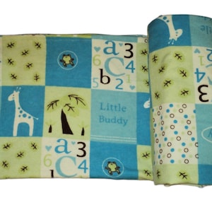 Peut inclure: Une couverture pour bébé bleu et verte avec un motif en patchwork. La couverture représente une girafe, une grenouille et les mots "Little Buddy".