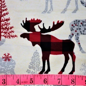 May include: Red and black plaid moose silhouette on a white background with grey and red trees and snowflakes. The image includes a pink measuring tape with inches marked.