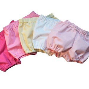 This is five pairs  bloomers that match the bonnets. They  are on an angle and overlapping in an arc like a rainbow. They have elastic at the waist the thigh. Colors left to right are bright pink, medium pink, yellow, white, and light pink.