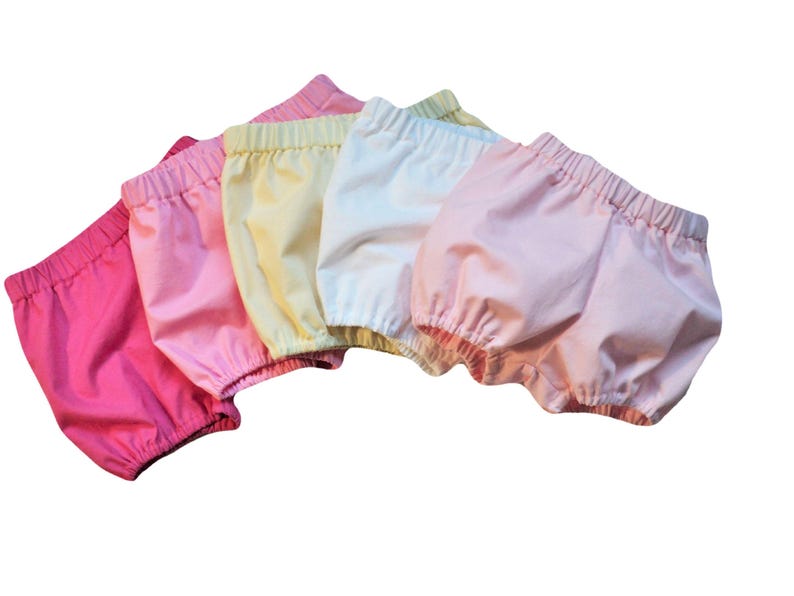 This is five pairs  bloomers that match the bonnets. They  are on an angle and overlapping in an arc like a rainbow. They have elastic at the waist the thigh. Colors left to right are bright pink, medium pink, yellow, white, and light pink.