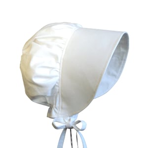 Prairie bonnet with wide brim facing right. It is solid white. The side-back is puffy and gathered onto the brim. There is a gathered ruffle at the bottom back. A white bow is tied under the hat with ties hanging down.
