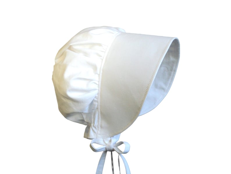 Prairie bonnet with wide brim facing right. It is solid white. The side-back is puffy and gathered onto the brim. There is a gathered ruffle at the bottom back. A white bow is tied under the hat with ties hanging down.