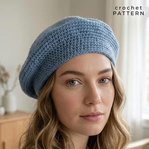 Könnte beinhalten: Ein hellblaues Häkelbarett. Das Barett ist aus einem strukturierten Garn gefertigt und hat eine klassische, runde Form. Der Text "crochet PATTERN" befindet sich in der oberen rechten Ecke. Dieser handgefertigte Hut ist ein stilvolles Accessoire für jede Jahreszeit.