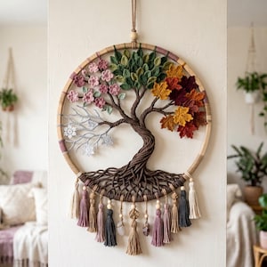May include: A circular wall hanging featuring a crocheted tree of life inside a wooden hoop. The tree displays four seasons with pink blossoms, green leaves, autumn-colored foliage, and white snowflakes. It includes hanging tassels and beads.