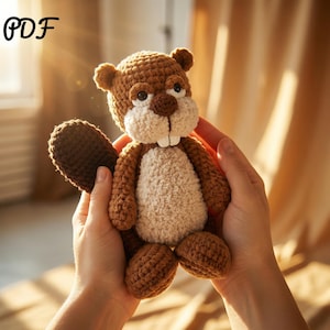 May include: A crocheted beaver toy in brown and cream colours. The beaver has a textured body, a flat tail, and two large white teeth. The image includes the text "PDF" in the upper left corner.