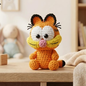 Könnte beinhalten: Handgemachtes orangefarbenes Garfield-Plüschtier aus Häkelarbeit mit schwarzen Streifen, schwarzen Ohren und einer rosa Nase. Das Häkeltier sitzt auf einer Holzoberfläche. Das Wort "PDF" befindet sich in der oberen linken Ecke.