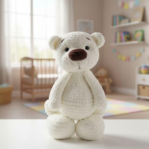 May include: A handmade, white crochet teddy bear with a brown nose and black eyes. The bear has a classic design with rounded features and is sitting upright. The background includes a crib and a colorful rug, suggesting a nursery setting.