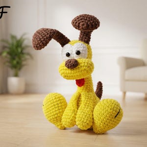 May include: A handmade, yellow crochet dog with brown ears, nose, and a tail. The dog has white eyes, a red tongue, and is sitting on a wooden floor. The word "PDF" is in the top left corner. The dog is a whimsical, decorative item.