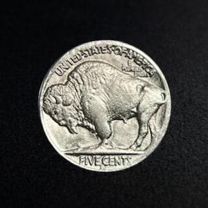 Puede incluir: Una moneda de níquel Buffalo de plata de los Estados Unidos. La moneda presenta una imagen detallada de un bisonte y las palabras "United States of America" y "Five Cents". La moneda está sobre un fondo negro.