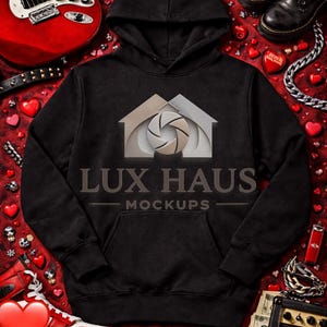 May include: Black hoodie with a front pocket and a hood, featuring the text "LUX HAUS MOCKUPS" and a logo. The image includes a red electric guitar, black boots, and heart-shaped decorations, creating a rock and roll theme.