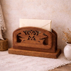 May include: A wooden letter holder with a carved design of birds and floral elements. The holder is stained a warm brown color and holds a cream-colored envelope. The design is a decorative and functional item for organizing mail.
