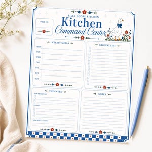 Könnte beinhalten: Ein weißer "Kitchen Command Center" Notizblock mit blauem und rotem Blumendesign. Der Notizblock hat Abschnitte für wöchentliche Mahlzeiten, eine Einkaufsliste, Top-Prioritäten, Aufgaben und Notizen. Eine Gänse-Illustration mit blauer Schleife befindet sich auf der rechten Seite.