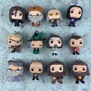 May include: A collection of miniature character figurines with keychains. The figures feature various characters with detailed facial features, clothing, and accessories. The figures are in various colors, including black, brown, and green.