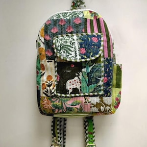 May include: A quilted backpack featuring a patchwork design with various floral and animal patterns in shades of green, pink, yellow, and white. The bag includes a front pocket with a flap, a top handle, and two adjustable shoulder straps.