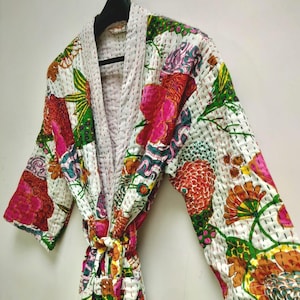May include: A long-sleeved robe featuring a white base with a vibrant, multi-colored floral and abstract pattern. The garment is constructed with visible running stitch quilting throughout and includes a matching tie belt at the waist.