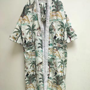 May include: A long-sleeved, open-front robe featuring a white base with a repeating jungle-themed print. The pattern includes green palm trees, yellow and black spotted leopards, zebras, and toucans. The garment has a quilted texture throughout.
