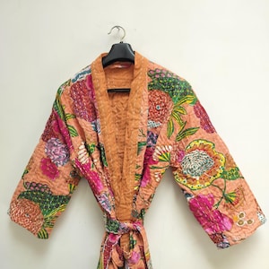 May include: A long-sleeved robe featuring a peach-colored base with a vibrant floral pattern in shades of pink, green, yellow, and orange. The garment has a quilted texture with visible white stitching throughout and includes a matching tie belt.