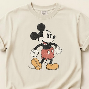 K&ouml;nnte beinhalten: Cremefarbenes T-Shirt mit einem Vintage-Mickey-Mouse-Motiv. Die Zeichentrickfigur ist in Schwarz, Rot und Gelb dargestellt, mit einem Used-Effekt. Das Shirt hat hochgekrempelte &Auml;rmel und der Text "COMFORT COLORS" ist oben links aufgedruckt.