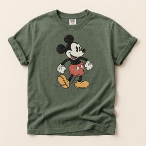 K&ouml;nnte beinhalten: Olivgr&uuml;nes T-Shirt mit einem Vintage-Mickey-Mouse-Motiv. Die Zeichentrickfigur ist in Schwarz, Wei&szlig;, Rot und Gelb dargestellt. Das T-Shirt hat hochgekrempelte &Auml;rmel und einen Rundhalsausschnitt. Das Etikett lautet "Comfort Colors".