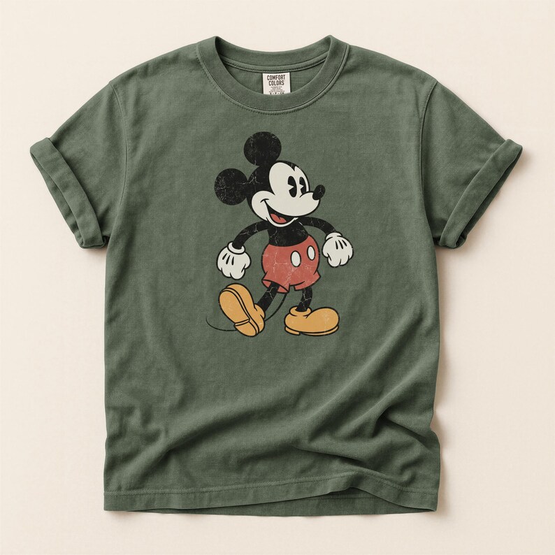K&ouml;nnte beinhalten: Olivgr&uuml;nes T-Shirt mit einem Vintage-Mickey-Mouse-Motiv. Die Zeichentrickfigur ist in Schwarz, Wei&szlig;, Rot und Gelb dargestellt. Das T-Shirt hat hochgekrempelte &Auml;rmel und einen Rundhalsausschnitt. Das Etikett lautet "Comfort Colors".