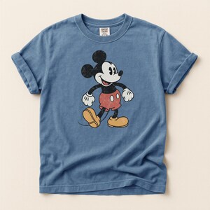 K&ouml;nnte beinhalten: Blaues T-Shirt mit einem Vintage-Mickey-Mouse-Design. Die Zeichentrickfigur ist in Schwarz, Wei&szlig;, Rot und Gelb gehalten. Das Shirt hat kurze &Auml;rmel und einen Rundhalsausschnitt. Das Etikett lautet "Comfort Colors".