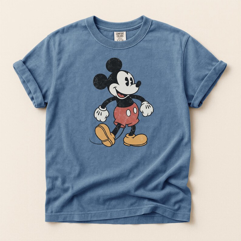 K&ouml;nnte beinhalten: Blaues T-Shirt mit einem Vintage-Mickey-Mouse-Design. Die Zeichentrickfigur ist in Schwarz, Wei&szlig;, Rot und Gelb gehalten. Das Shirt hat kurze &Auml;rmel und einen Rundhalsausschnitt. Das Etikett lautet "Comfort Colors".
