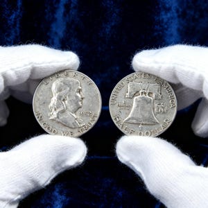 May include: Two silver 1952 Franklin half dollars. One coin shows Benjamin Franklin's profile and the words "LIBERTY" and "IN GOD WE TRUST." The other coin features the Liberty Bell and the words "UNITED STATES OF AMERICA."