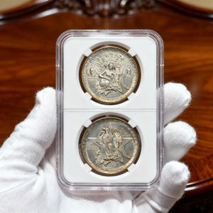 May include: Two 1957 silver half dollars in a clear protective case. The top coin features a seated woman with the words "INDEPENDENCE HALL" and "HALF DOLLAR". The bottom coin shows an eagle with a star and the words "UNITED STATES OF AMERICA".