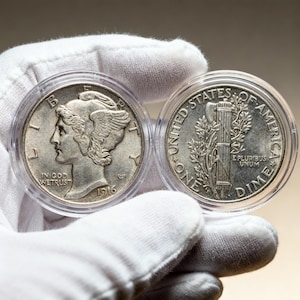 Könnte beinhalten: Zwei silberne Mercury Dimes in Schutzhüllen. Die Vorderseite einer Münze zeigt ein Profil mit dem Text "IN GOD WE TRUST" und dem Datum "1916". Die Rückseite der anderen Münze zeigt ein Rutenbündel und "ONE DIME".