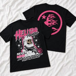 Könnte beinhalten: Ein schwarzes Kurzarm-T-Shirt mit einer Grafik eines Schädels in einem Astronautenhelm und dem Text HELLSTAR Adventure NEVER MIND JUST GO WITH THE FLOW AND TRUST THE JOURNEY. Die Rückseite zeigt ein rosa kreisförmiges Logo mit einem Flammendesign.