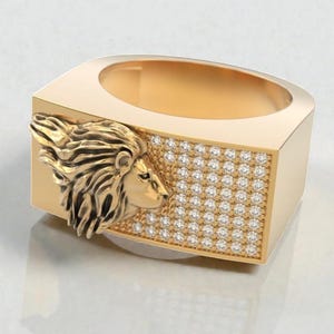 May include: A gold-colored ring with a lion's head on the side and a rectangular face covered in small, sparkling stones. The ring has a modern, geometric design and a polished finish.