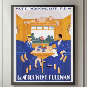 Op de afbeelding: Een ingelijste vintage reisaffiche met de tekst "LONDRES.VICHY.PULLMAN" en "NORD.WAGONS.LITS.P.L.M" toont een interieurscène van een trein. De poster wordt weergegeven boven een bruine leren fauteuil en een kleine bijzettafel met een plant.