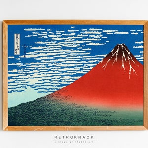 May include: A framed print of a Japanese woodblock print depicting Mount Fuji with a red mountain and white snow against a blue sky with white clouds. The print has Japanese text in the upper left corner.