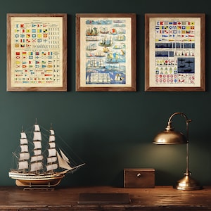 May include: Three framed vintage nautical charts with signal flags and ship illustrations. A model sailing ship and a brass desk lamp sit on a wooden desk, creating a maritime theme. The desk is made of wood.
