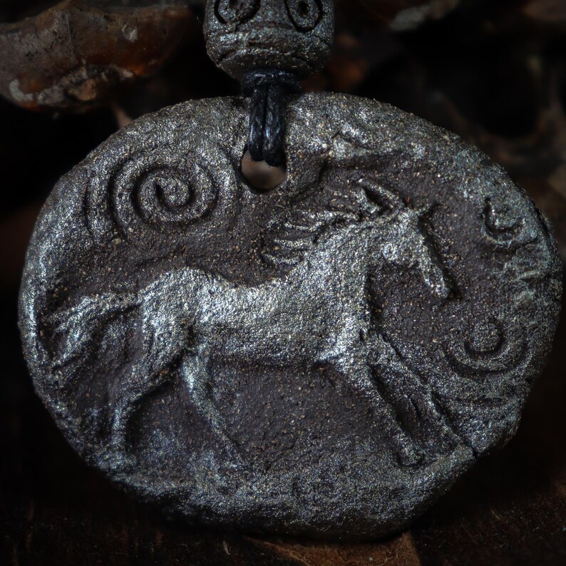 May include: A dark gray, oval-shaped pendant featuring a textured, embossed horse figure in the center. The surface has a metallic, shimmering finish with spiral patterns on the sides. A black cord passes through a hole at the top, secured by a bead.