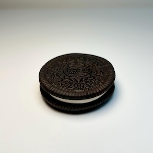 May include: A close-up shot of an Oreo cookie. The dark chocolate wafers sandwich a thick layer of white cream filling. The top cookie has the word "OREO" embossed in the center.