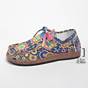 May include: A pair of patterned slip-on shoes with a colourful design. The shoes have a blue base with a repeating pattern of orange, yellow, and green shapes. The sole is brown, and the laces are rainbow-coloured. The sole is 2.5cm high.