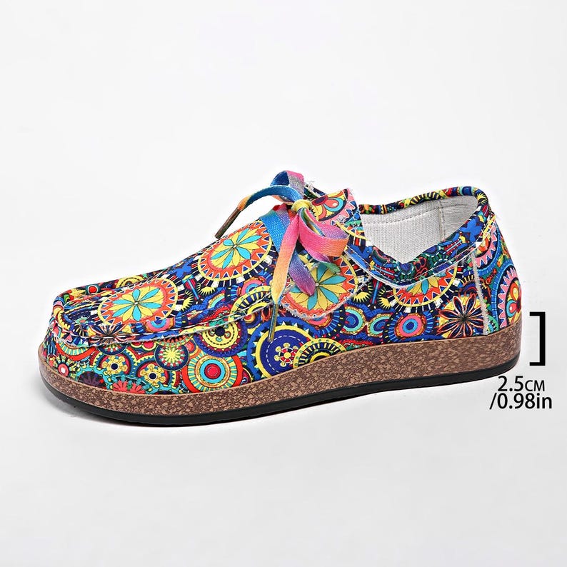 May include: A pair of patterned slip-on shoes with a colourful design. The shoes have a blue base with a repeating pattern of orange, yellow, and green shapes. The sole is brown, and the laces are rainbow-coloured. The sole is 2.5cm high.