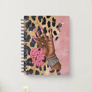 May include: Spiral-bound notebook with a cover featuring a hand with long pink nails, a watch, and bracelets. The background has a leopard print pattern and a pink section. The text "Clock That Tea" is displayed in pink.