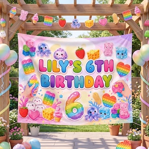 May include: A rectangular birthday banner featuring the text LILY'S 6TH BIRTHDAY in colorful letters, surrounded by illustrations of squishy toys, strawberries, octopuses, cheese, and a large rainbow-colored number 6 on a pastel background.