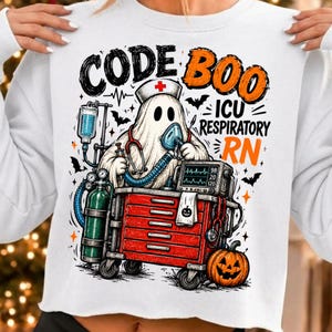 Puede incluir: Una sudadera blanca con el gráfico de un fantasma que lleva una cofia de enfermería y un estetoscopio, sosteniendo una máscara de oxígeno. El diseño incluye un carro médico rojo, un tanque de oxígeno verde, una calabaza y el texto CODE BOO ICU RESPIRATORY RN.