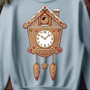 May include: A light blue crewneck sweatshirt featuring a central graphic of a brown gingerbread cuckoo clock. The clock design includes a small bird at the top, a white clock face with black numbers, and two hanging pinecone-shaped weights.