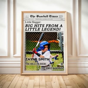 May include: A framed newspaper print titled "The Baseball Times" featuring a young baseball player. The headline reads "Little Slugger: BIG HITS FROM A LITTLE LEGEND!" The player, Zayne Smith, is wearing a blue helmet and holding a bat.