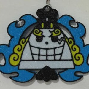 May include: A keychain featuring a stylized, grinning skull with a black top, blue wavy accents, and yellow details. The skull has a white face with black outlines and a large, toothy grin. The keychain is hanging from a silver chain.