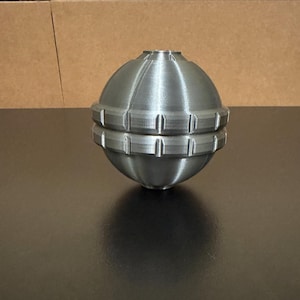 May include: A white ceramic mug with a black handle and the text "But First, Coffee" in a bold, black font. The mug is set against a blurred background, highlighting its simple design.