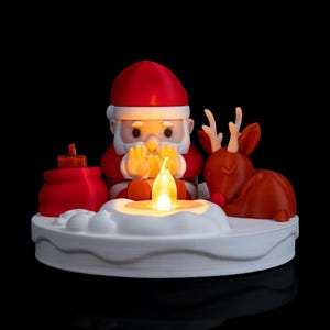 May include: A 3D printed decorative figurine featuring a red and white Santa Claus sitting with hands near a glowing yellow LED flame, a red gift sack, and a brown reindeer on a white circular base with a snow-like texture.