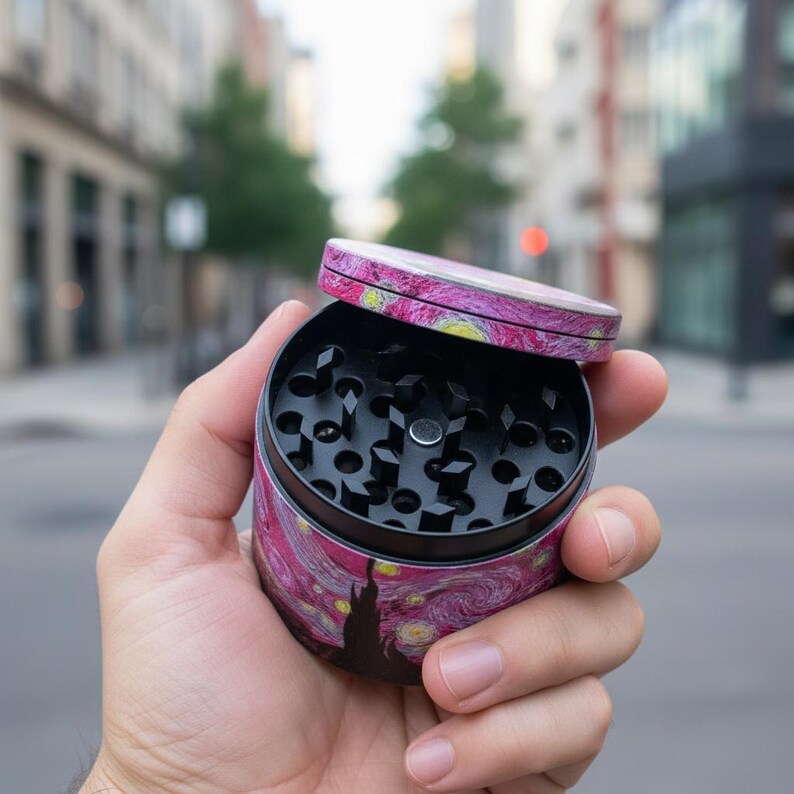 May include: A round, two-piece herb grinder with a lid. The grinder features a vibrant, artistic design inspired by Van Gogh's "Starry Night" painting, with swirling pink, yellow, and blue colors. The interior is black with sharp teeth for grinding.