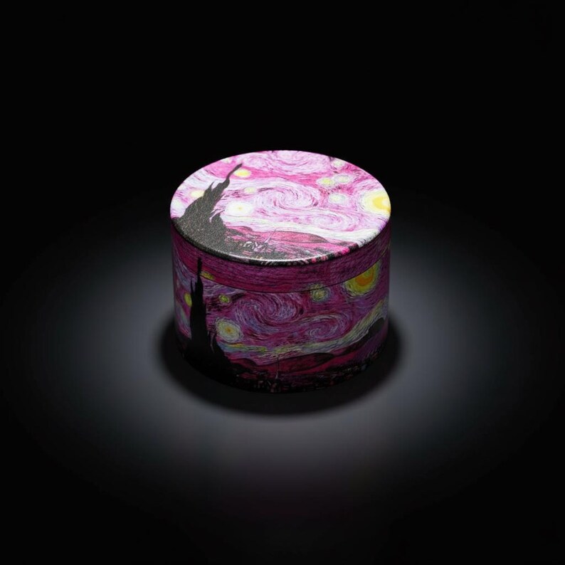 May include: A cylindrical box featuring a print of Van Gogh's "Starry Night" painting. The box has a pink and purple swirling sky design with yellow stars and a black silhouette of a town. The box is set against a black background.