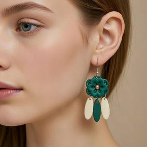 May include: Dangle earrings with a dark green flower design and a copper-coloured centre. The earrings have two off-white and one dark green teardrop-shaped pendants. The earrings are suspended from silver-coloured hooks.